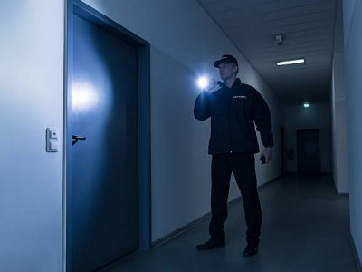 Full length of mature security guard with flashlight standing in front of door in building
